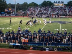 How Many Players Are on a High School Football Team? High school football players on the field during a game, with teammates and coaches watching from the sideline