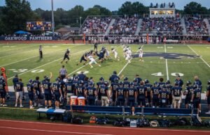 How Many Players Are on a High School Football Team? High school football players on the field during a game, with teammates and coaches watching from the sideline
