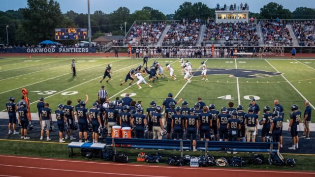 High School Football Team on Game Day High school football players on the field during a game, with teammates and coaches watching from the sideline
