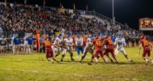 How Many Kids Play High School Football in the US? High school football players competing under Friday night stadium lights in front of packed bleachers in the United States.