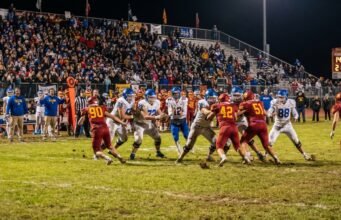 How Many Kids Play High School Football in the US? High school football players competing under Friday night stadium lights in front of packed bleachers in the United States.