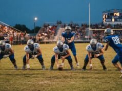 How Many Quarters Are in a High School Football Game? Full Breakdown High school football players lined up at the line of scrimmage under Friday night lights with the scoreboard clock visible